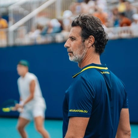 Patrick mouratoglou observing a player during a match on a blue court.